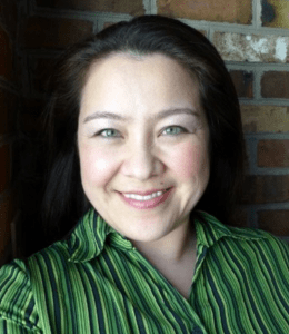 Wren Fritsky headshot, wearing a green and black striped shirt in front of a brick background