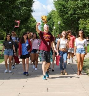 Male orientation leader shakes pom-pom as he leads a tour around campus.