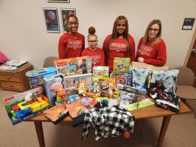 A group of people standing behind a table filled with items. 