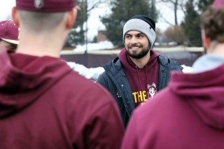 Students and assistant baseball coach talking outside in the winter. 