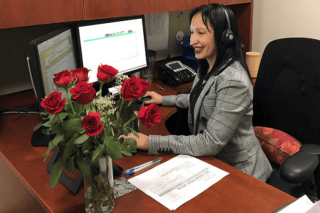 A woman sitting at a desk, admiring flowers. 