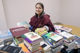 A girl sitting with a stack of books. 