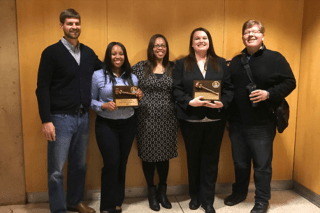 A group of five standing side by side with awards. 