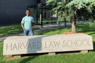 A man standing behind a Harvard Law School sign.