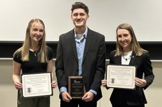 Three people standing with awards. 