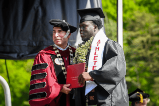 Two people standing on a stage, both holding a diploma. 