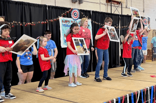 A group of kids standing next to each other. Each child is holding a picture. 