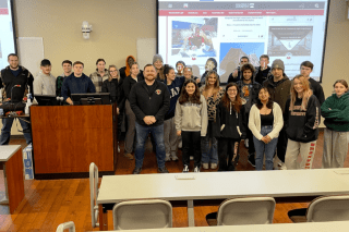 A group of people standing in a classroom in front of a projector. 