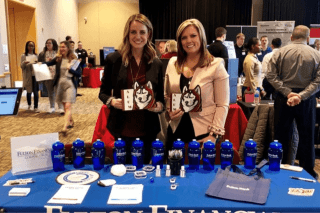 Two girls standing behind a vendor table. 