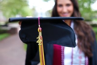 A graduation cap being held out by a girl. 