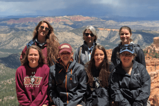 Seven women standing together with a mountain behind. 