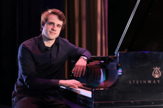 A man sitting by a piano. 