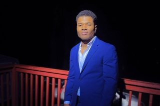 Marvens Ravix in a dark blue suit in front of a red railing. 