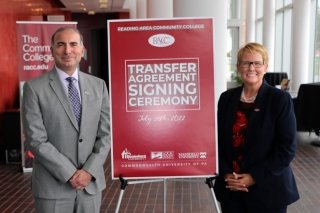 Two people standing next to the transfer agreement signing ceremony sign.