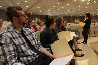 A group sitting in chairs with folders. 