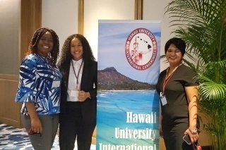 Three people standing by a Hawaii sign.