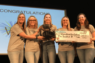 Five people standing on a stage holding a large check. 