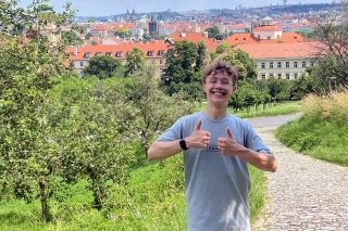 A man, with two thumbs up, standing on a gravel path, with trees in the background. 