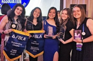 Five girls wearing dresses, all holding awards. 