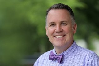 A headshot of a man wearing purple. 