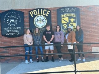 Group of students standing in front of 3 Police signs. 