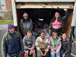 Students standing and sitting at the end of a box truck. 