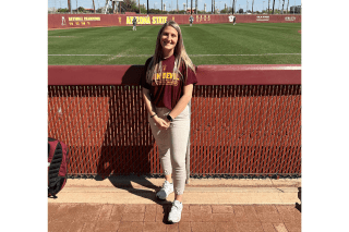 A woman standing by a baseball field. 