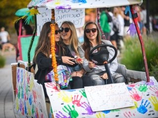 Three girls on a golf cart decorated with colorful handprints.