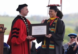 Two people standing on a stage. One person handing an award to another person. 