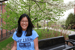 A girls standing in front of a bench outside. 