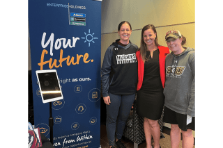 Three people standing side by side next to a your future sign. 