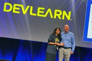 Two people standing in front of a DEVLEARN sign. 