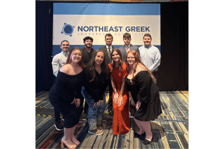 A group of people standing in front of a Northeast greek sign. 