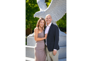 Two people standing side by side in front of a statue. 