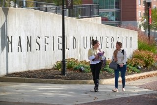 Two students walking by the Mansfield wall. 