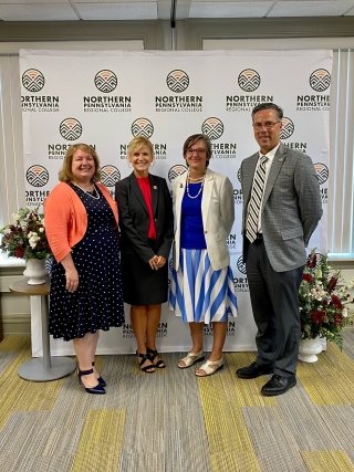 A group of four standing together in front of a photo background wall.