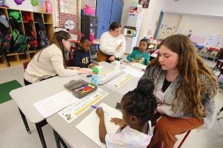 Education major students sitting and helping elementary students. 