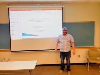 Justin Crowl standing in a classroom by a projector screen. 