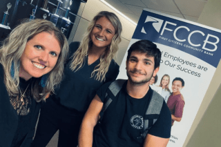 A group of people standing by an FCCB sign. 