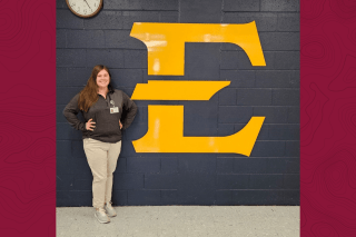 A girl standing next to an E on the wall. 