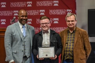 Three people standing together with an award. 