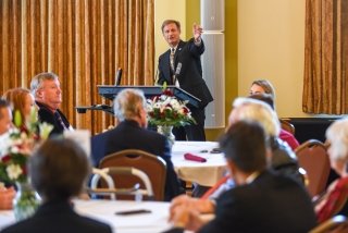 A speaker, at a podium, talking to a group of people. 