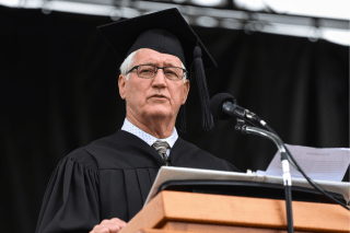 Photo of  Dan Cruttenden in graduation garb, speaking at a podium