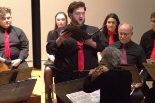 A CU-Mansfield music student singing on stage under direction with other vocalists surrounding him