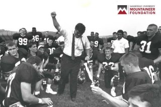 Football coach Tom Elsasser pumps fist in air with Mountaineer players surrounding. Logo says Mansfield University Mountaineer Foundation