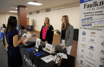 Two Bloomsbury alumnis standing behind a Faulker booth table talking to a student.