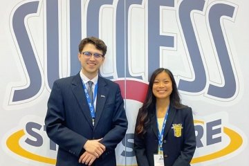 Two people standing in front of a success sign. 
