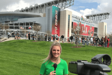 A woman with a microphone standing in front of a large building. 