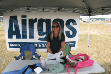 A woman standing behind a vendor table. Her sign says, "Airgas."