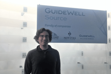 A man standing in front of a Guidewell source sign. 